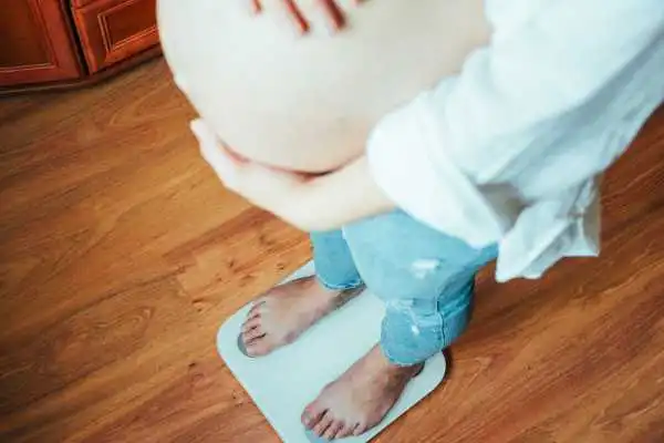 Image of woman weighing herself and experiencing weight gain through pregnancy Mansfield